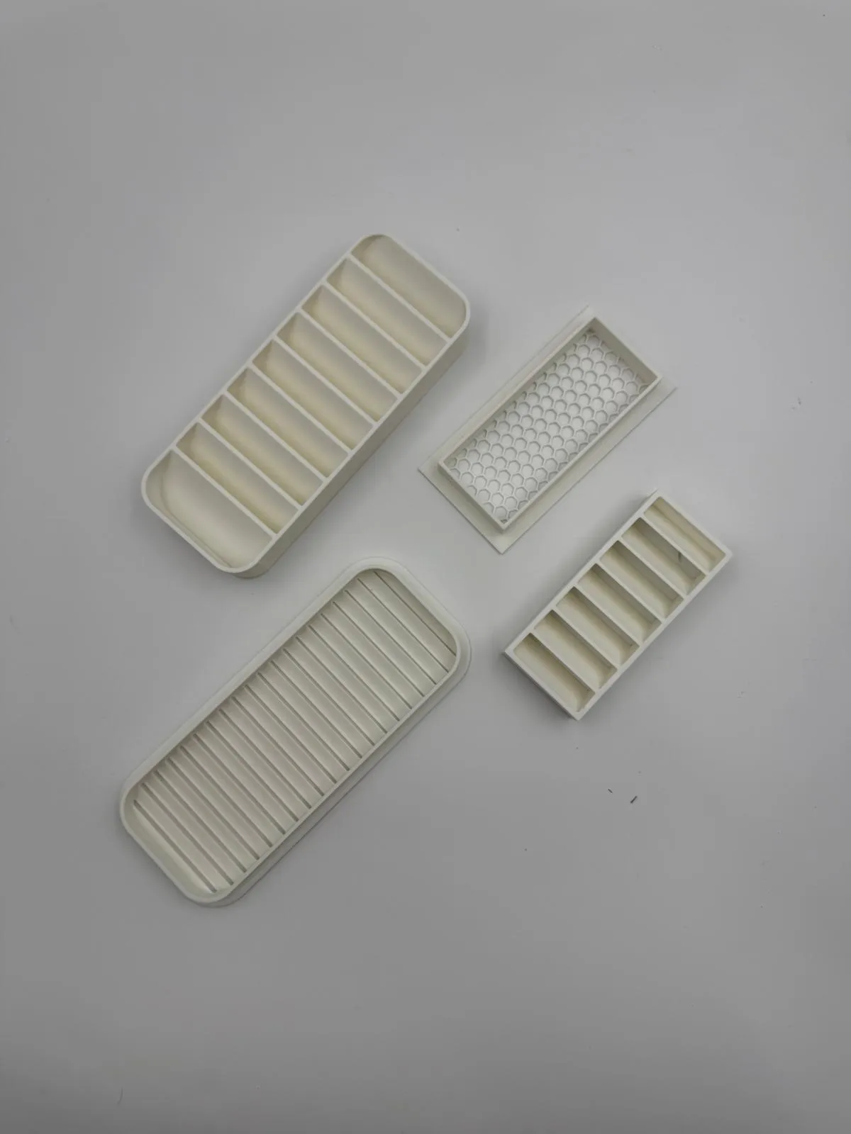 Top-down view of one set of white vent parts: the angled louvre, the large straight-slat vent, the small honeycomb vent and the horizontal louvre