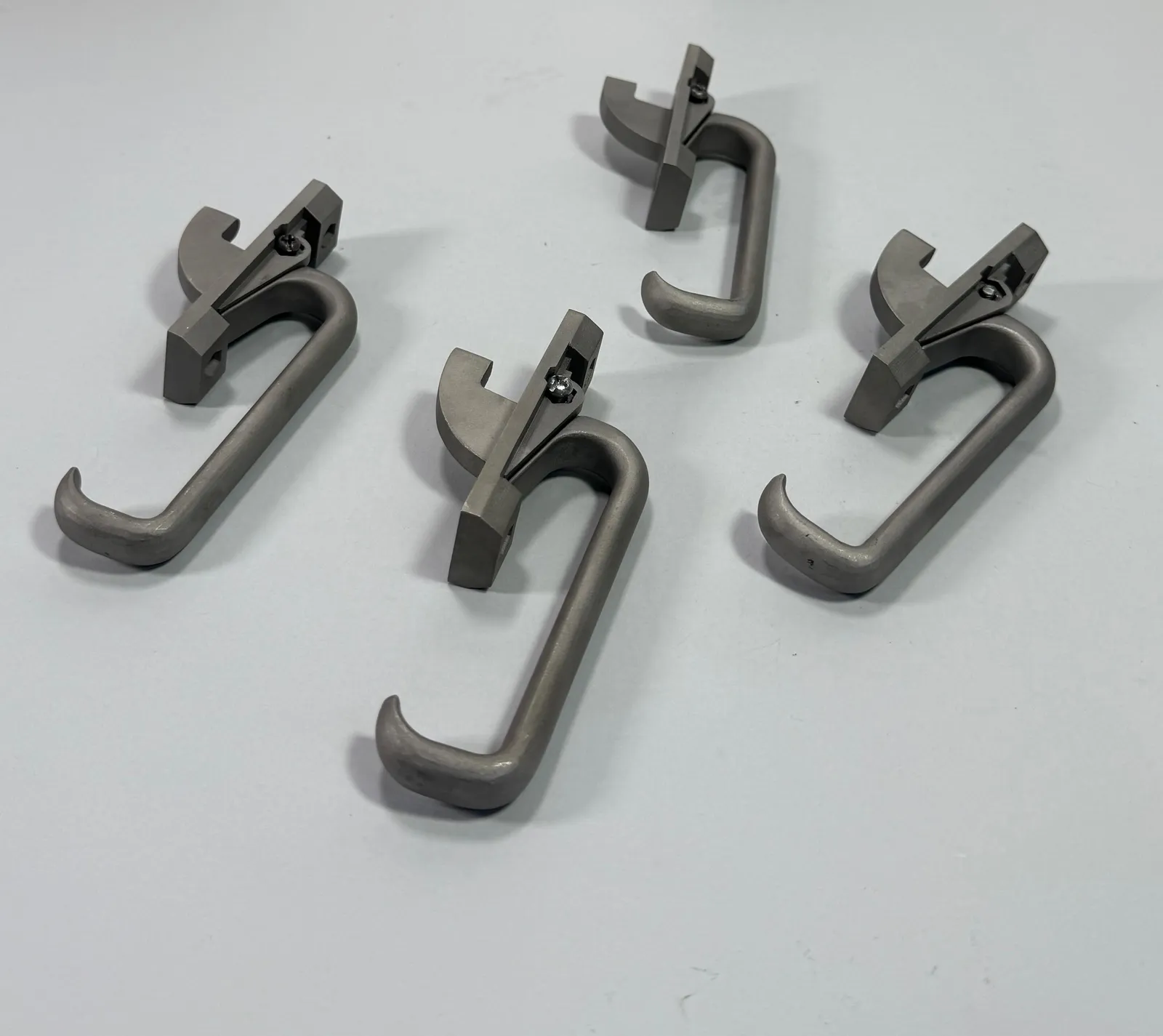 The four finished latches lying in a loose group on a pale table, seen at an angle with each catch and screw facing up
