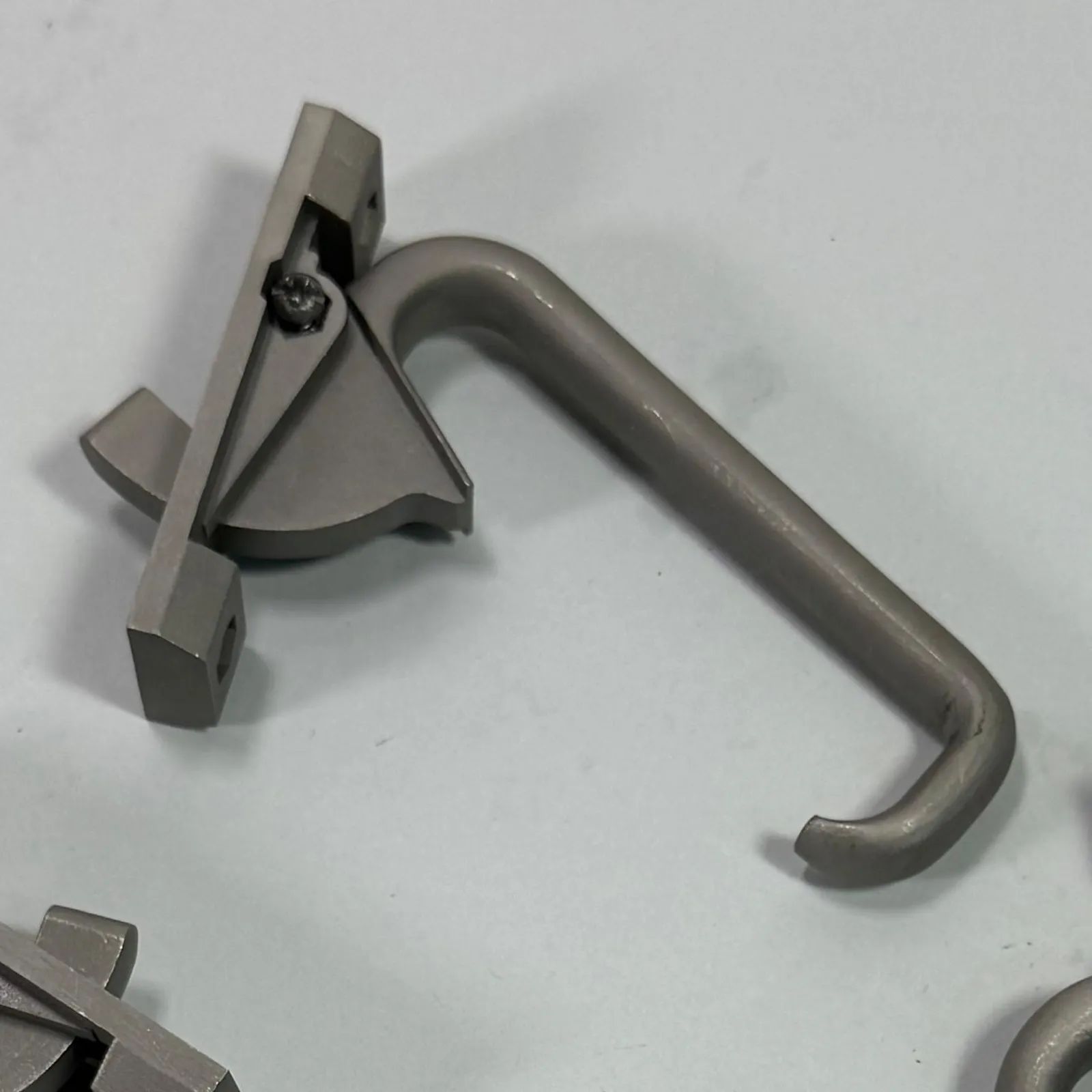 Close-up of one finished latch: the catch with its curved lip, the screw at the pivot and the start of the hooked handle