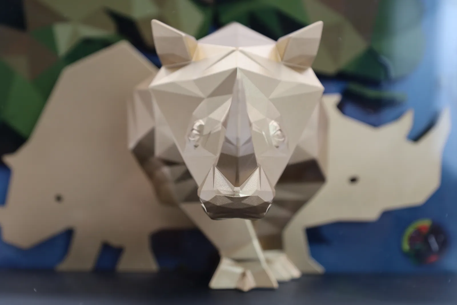 The gold low-poly rhino seen head on, in front of the pale gold cut-out rhinos of the backdrop