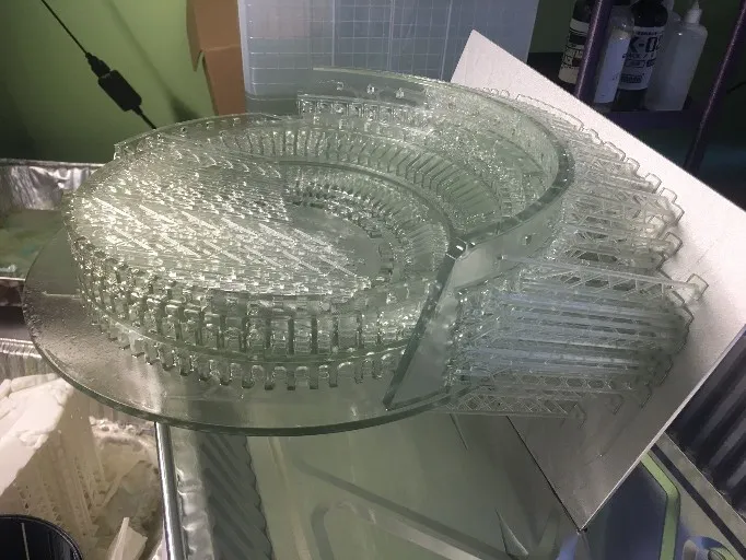 The clear Colosseum on its round base just off the printer, with a block of thin supports still attached along one side