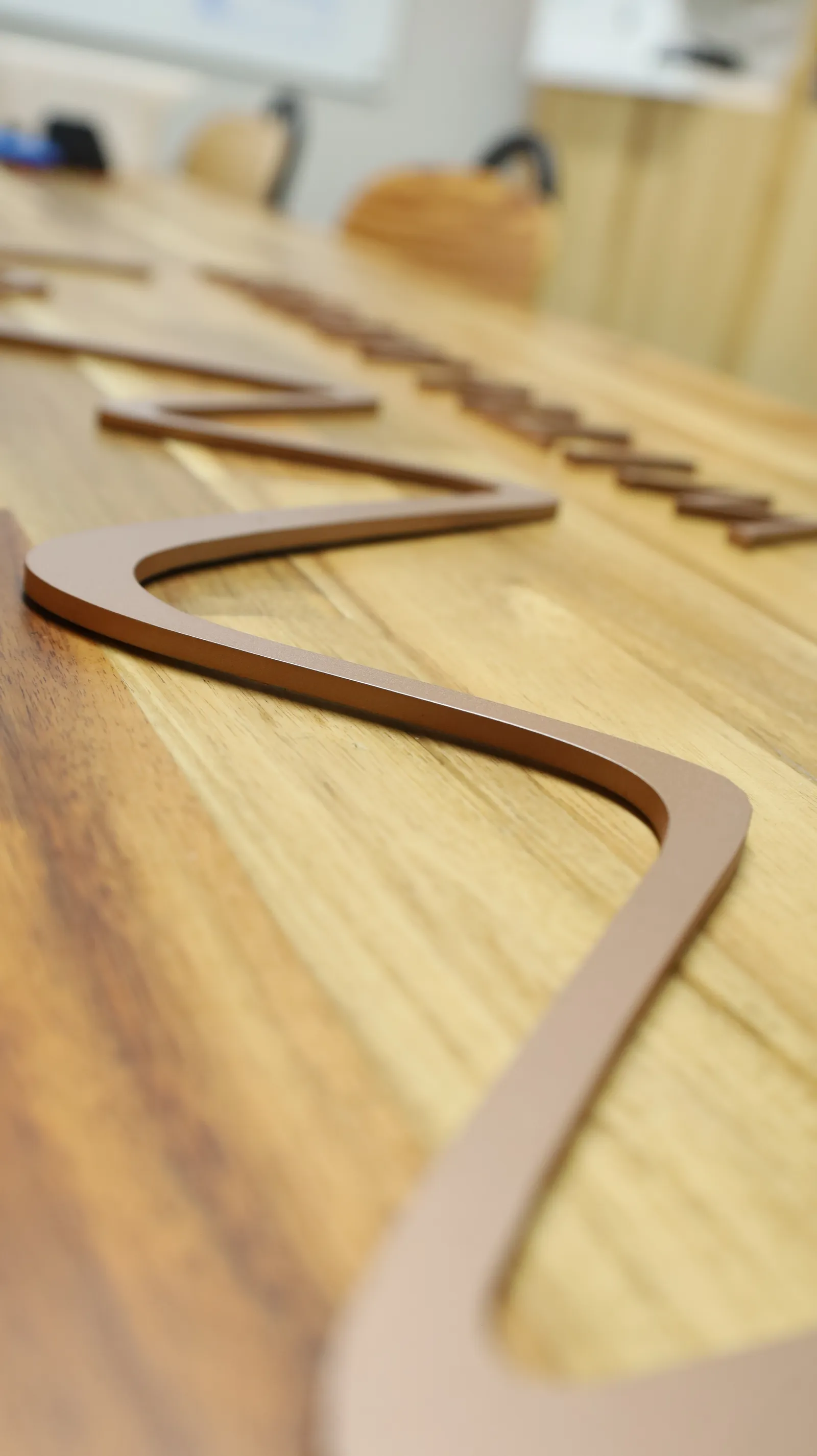 Close up of the rose gold logo mark lying on a table, showing the smooth curves and the 5 mm thick painted edge