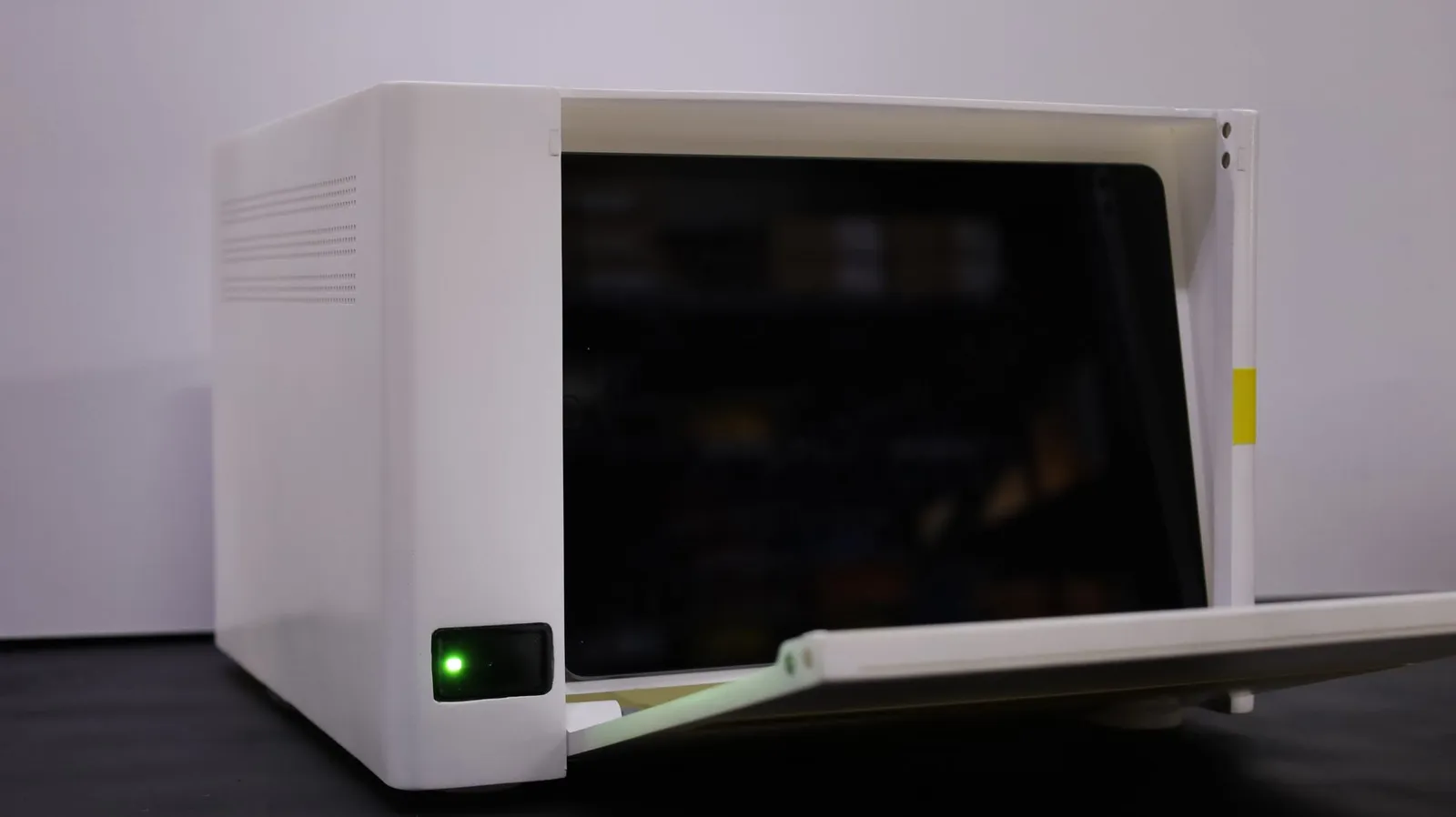 The Incucyte CX3 model with its front folding down, the dark screen behind it and the green status light at the lower left