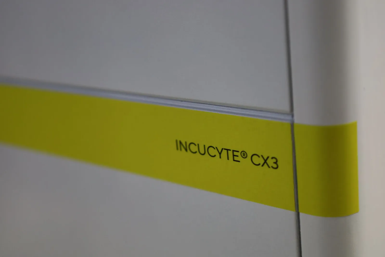 The yellow band on the front of the Incucyte CX3 model, printed INCUCYTE CX3