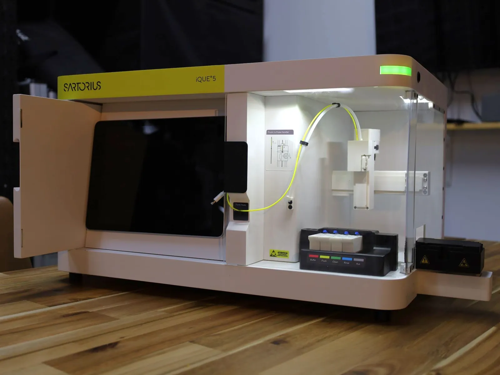 The iQue 5 model with its front door open: the screen on the left, and the lit bay on the right with the probe arm, yellow tubing and the four reagent bottles in their holder