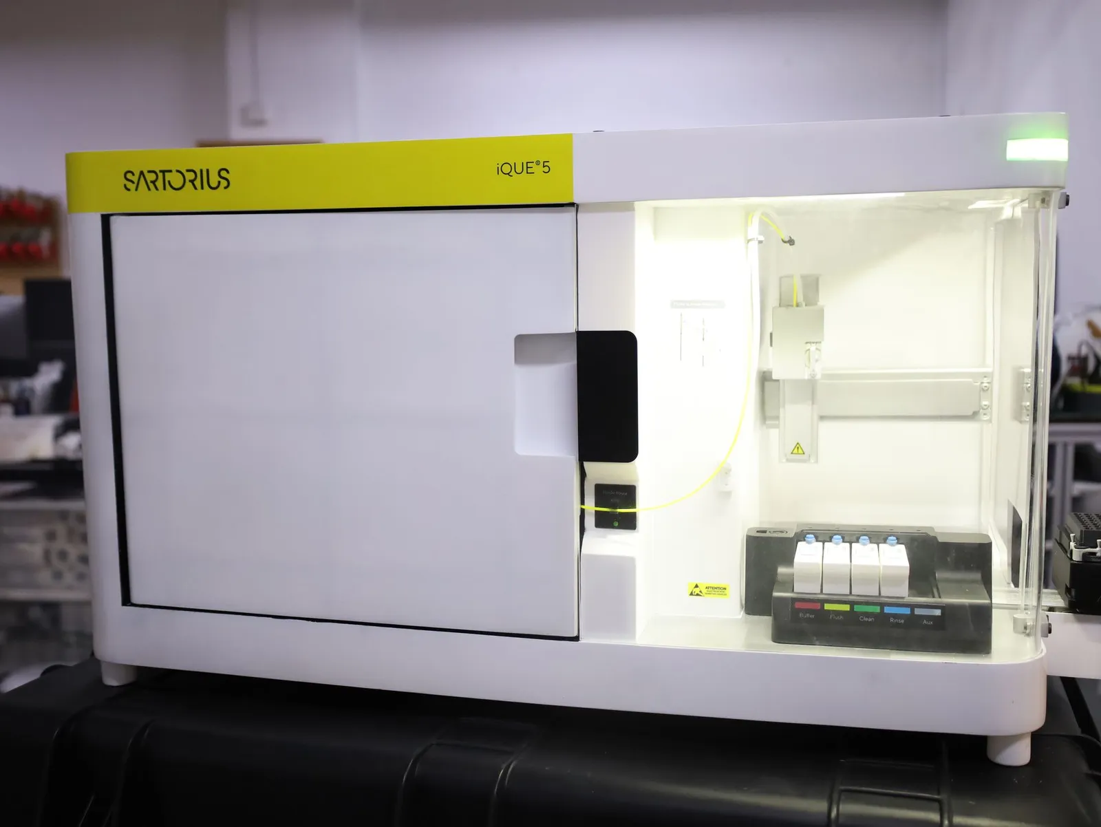 The iQue 5 model with its front door closed, the yellow Sartorius band along the top and the lit bay on the right showing the probe arm and reagent bottles