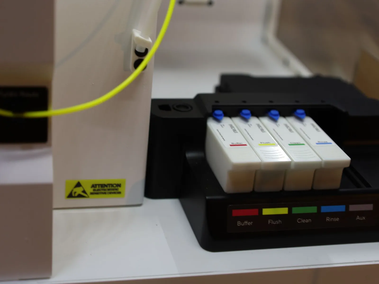 The iQue 5 model's four white reagent bottles with blue caps in their black holder, with red, yellow, green, blue and grey colour bars along its front