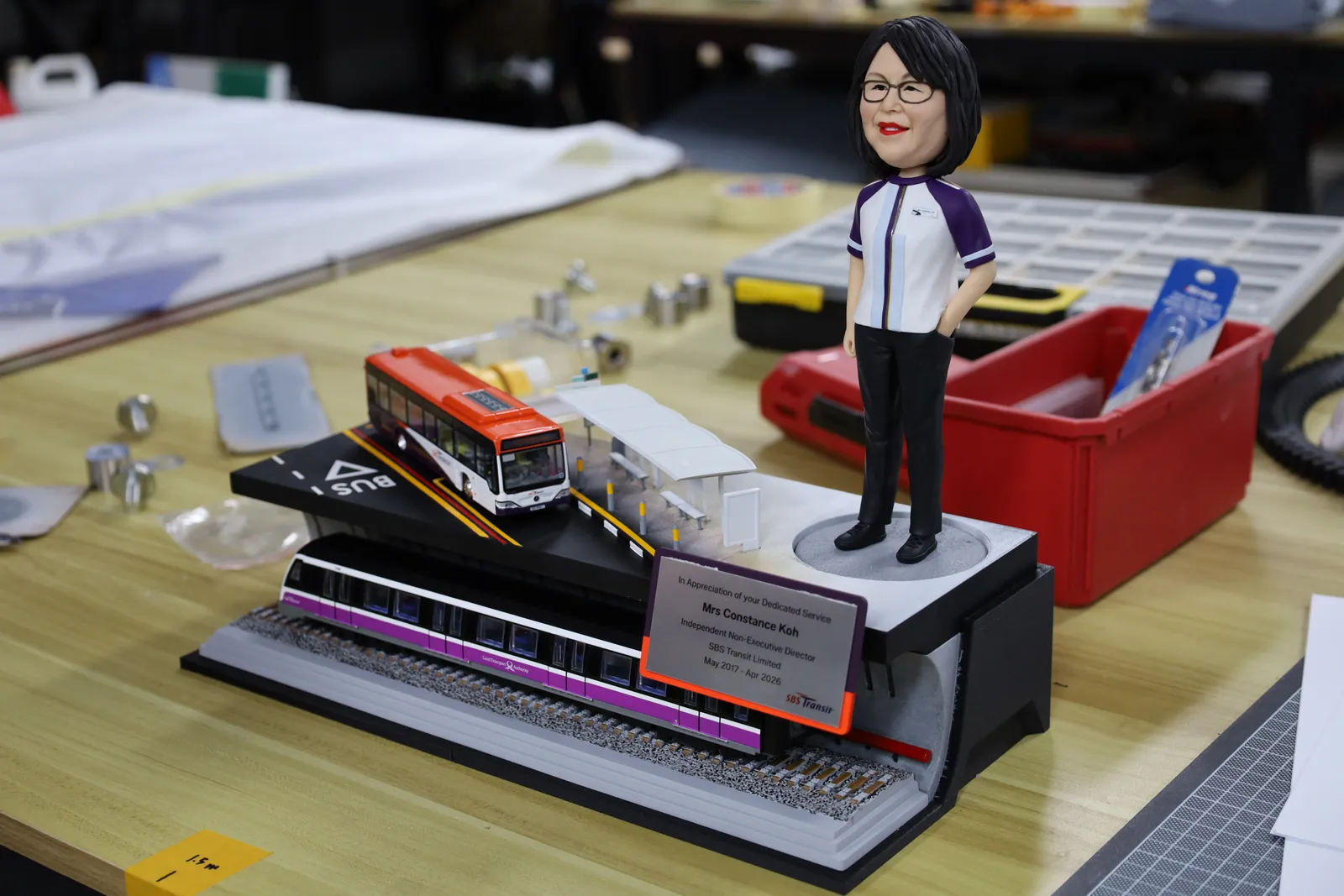 The trophy nearly complete on the workbench, with the bus, train and name plate in place and the figurine on a stand beside it