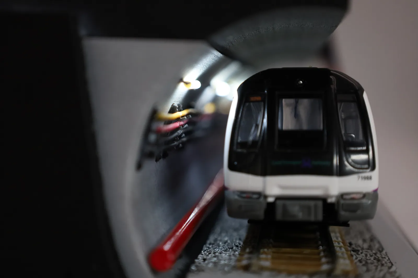 An MRT train seen head-on inside the curved tunnel, with small lights glowing along the tunnel wall
