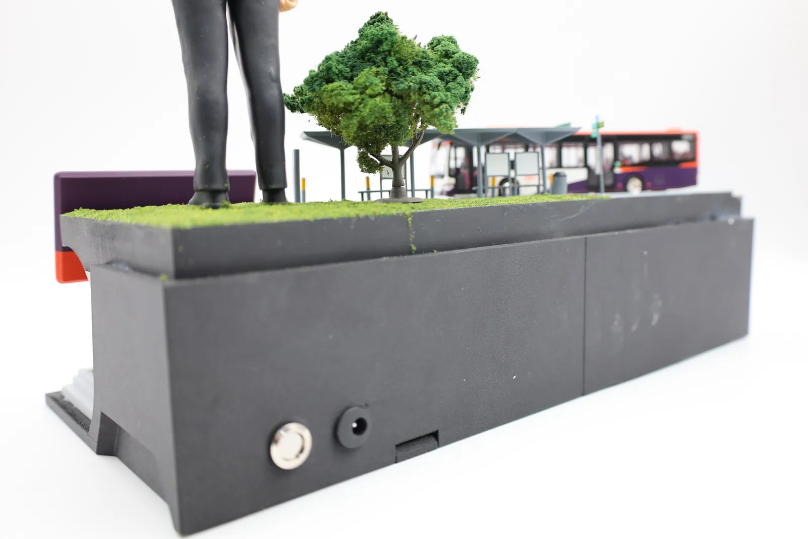 The side of the trophy base with a round switch and a power socket, flocked grass and a model tree on top