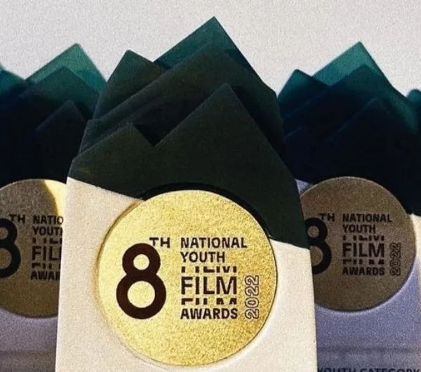 Close-up of a trophy top: layered translucent teal peaks above a gold disc reading 8th National Youth Film Awards 2022, set into the white tower