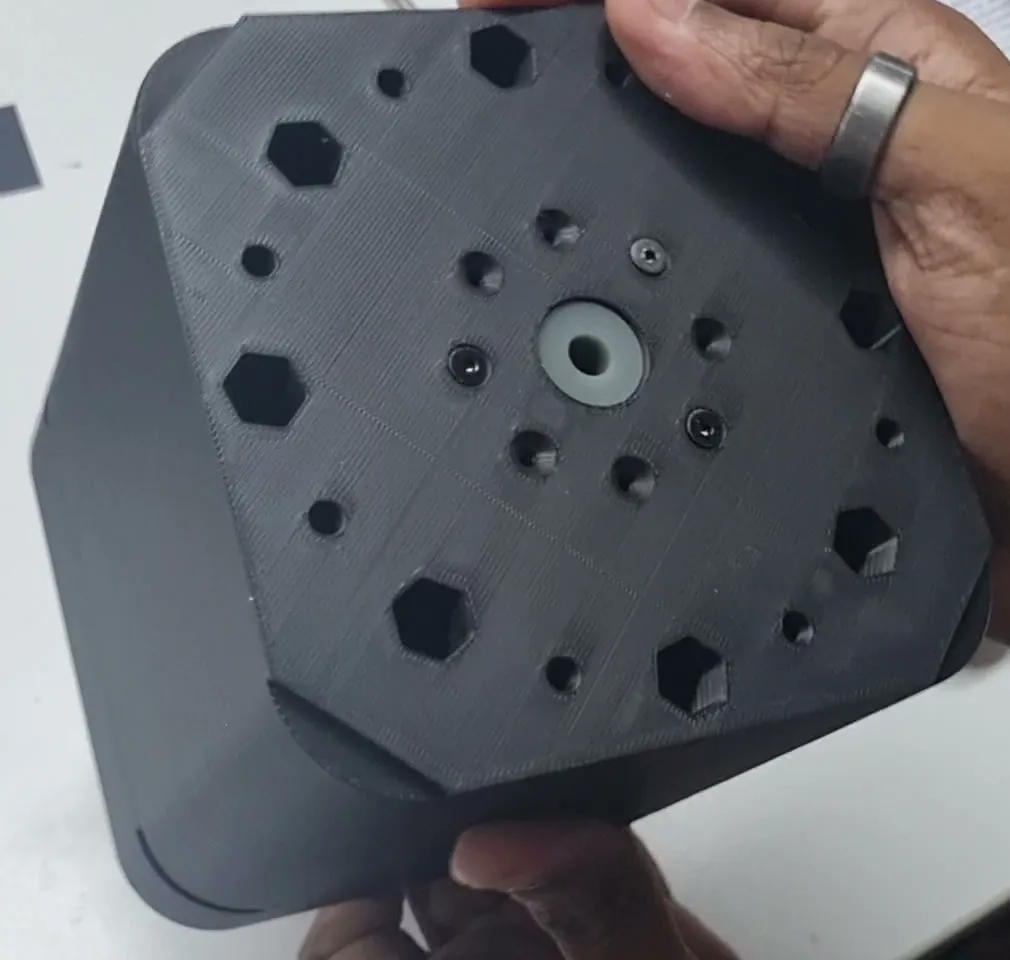 The sprue face of the cup mould held up to the camera: the grey resin sprue insert at the centre, ringed by bolt holes and hexagonal pockets