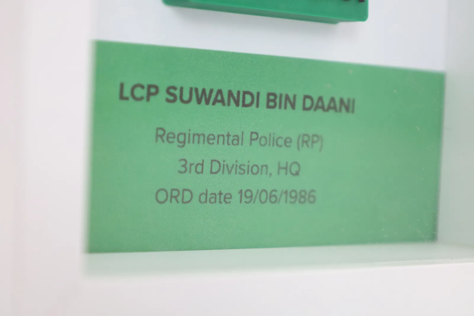 Close-up of the green name card: LCP Suwandi bin Daani, Regimental Police (RP), 3rd Division, HQ, ORD date 19/06/1986