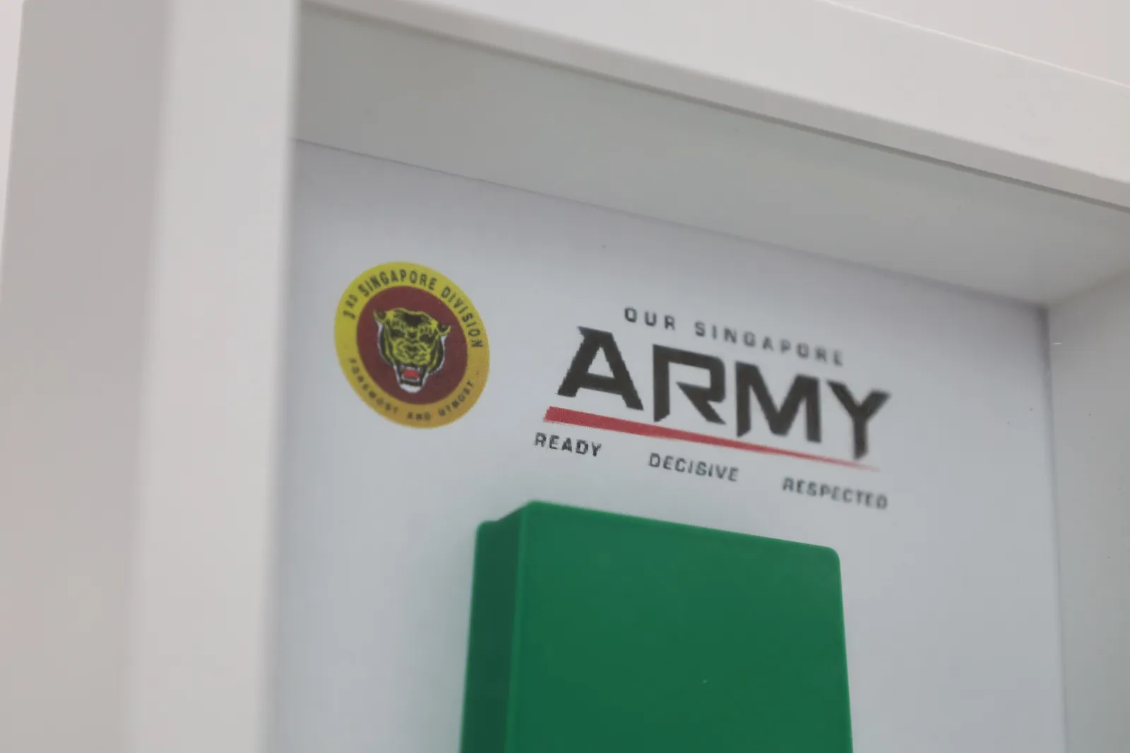 Inside the shadow box: the 3rd Singapore Division tiger crest and the Our Singapore Army logo on the white backing, above the top of the green slide