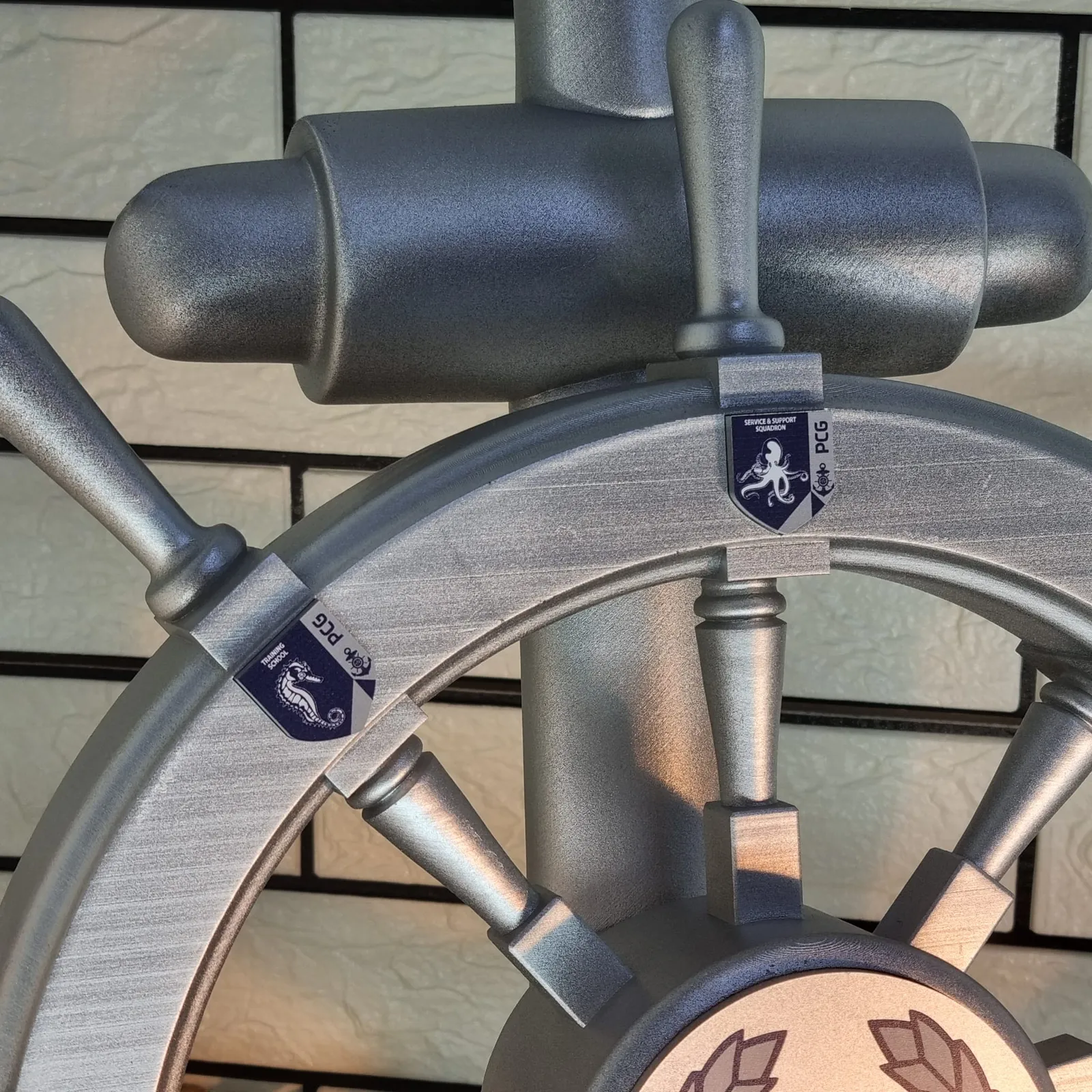 Close-up of two blue PCG unit badges on the silver rim, a seahorse for the Training School and an octopus for the Service and Support Squadron
