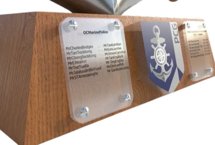 Close-up render of the wooden base with clear acrylic name plaques screwed on either side of the blue PCG shield