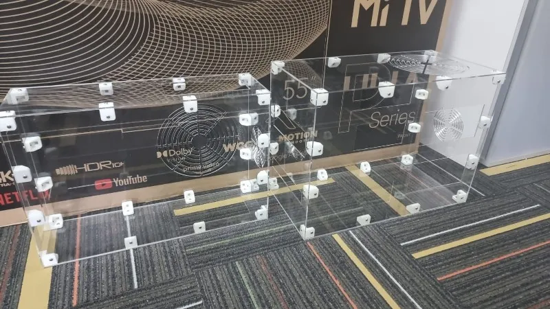 Both finished clear acrylic boxes side by side on an office carpet, white brackets along every edge and fan grilles in the panels
