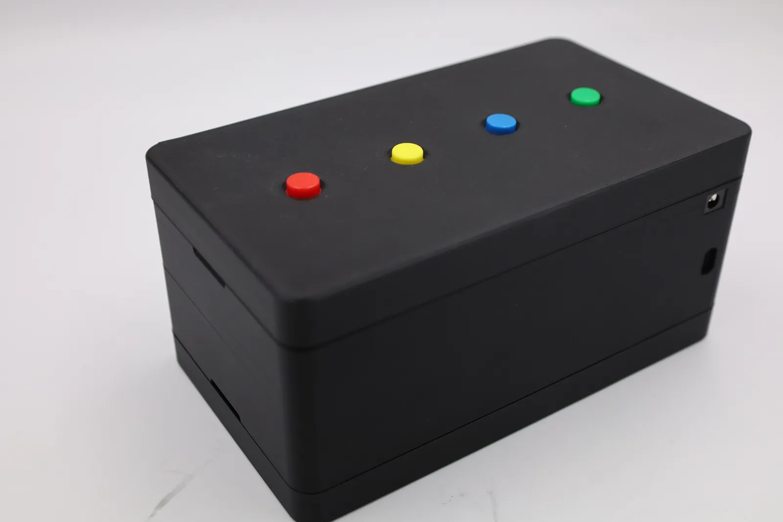 The black 3D printed response box with its push-button lid on, four round buttons in red, yellow, blue and green, and power and USB-C ports in the end wall