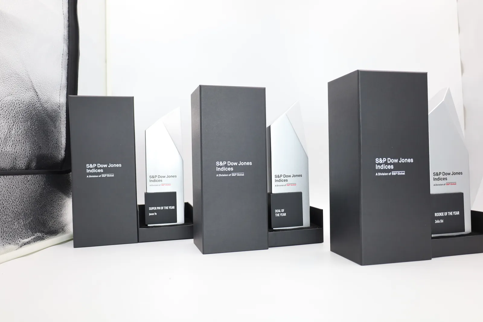 Three finished trophies standing in the base trays of their black gift boxes, each lid printed with the S&P Dow Jones Indices logo