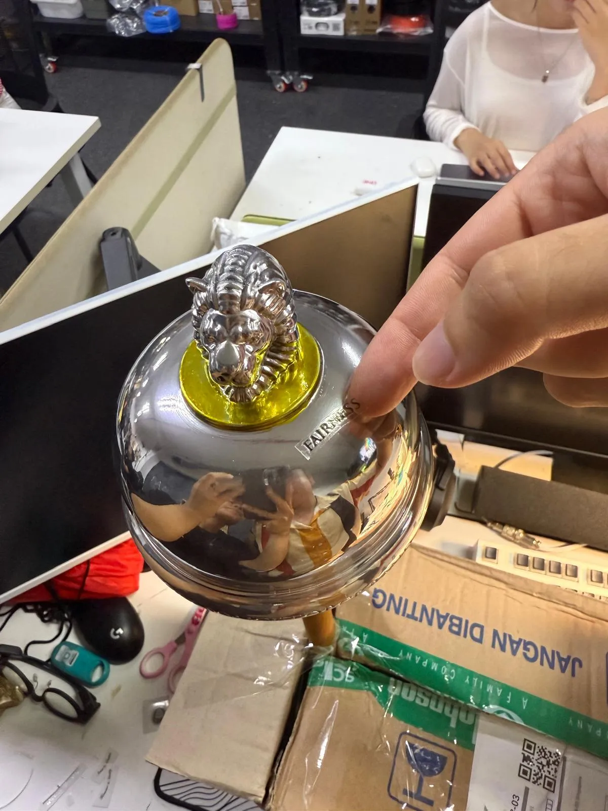 The chrome mace head held up in the workshop: a silver lion on a gold disc above a mirror dome lettered FAIRNESS