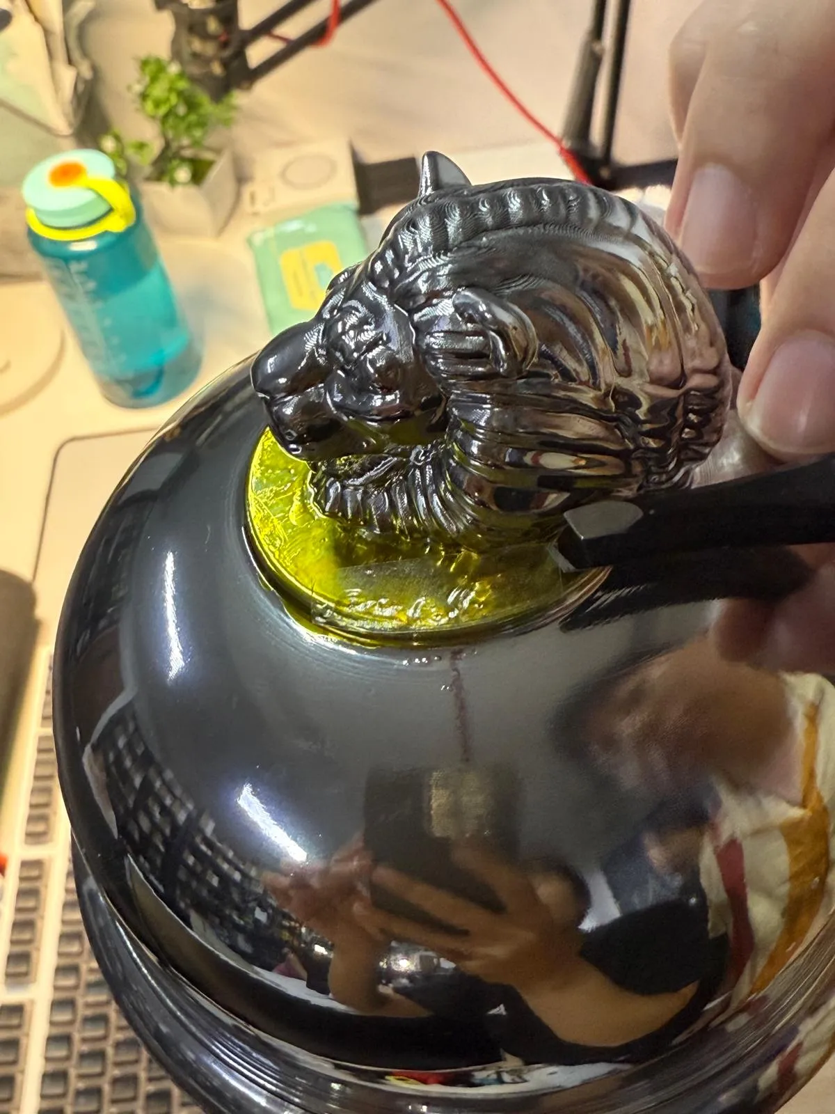 Close-up of the chrome lion on its gold disc, a fine tool resting at its base, the workshop reflected in the mirror dome