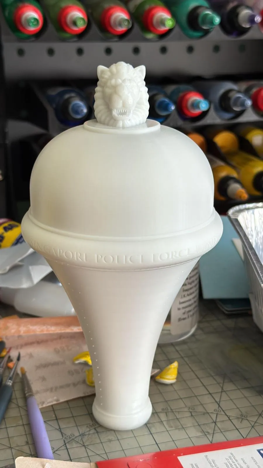The printed mace head in plain white on a cutting mat: a lion on top of a round dome, SINGAPORE POLICE FORCE lettered round the rim and a tapered neck below