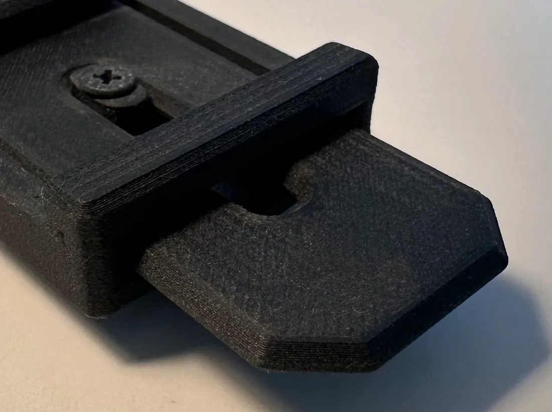 Close-up of the printed latch tongue standing out from the end of the rail, its chamfered tip and the matt carbon-fibre texture