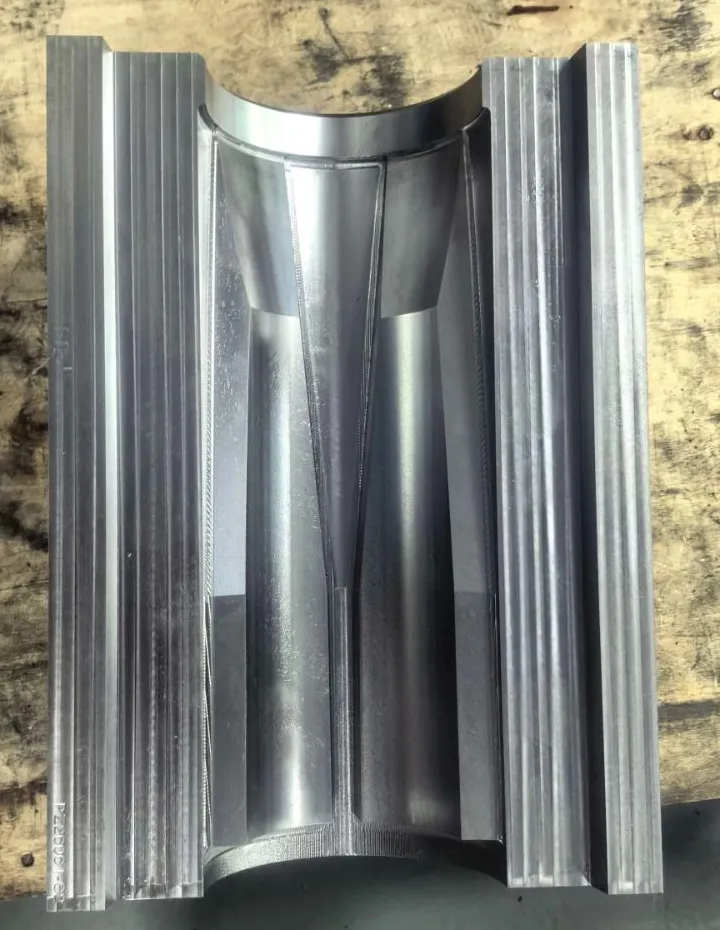 One machined steel half of the mould on a workbench: a curved cavity with the sleeve's tapered channels cut into it