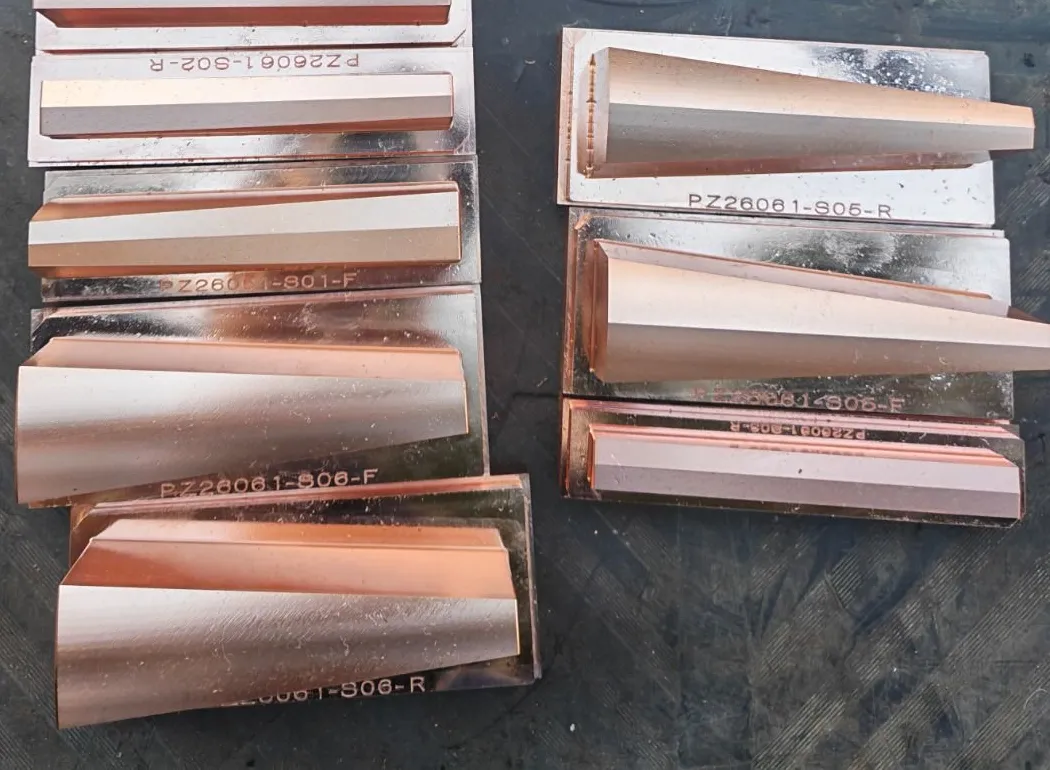 Machined copper electrodes laid out in two rows, each engraved with its part number, shaped to the sleeve's tapered channels