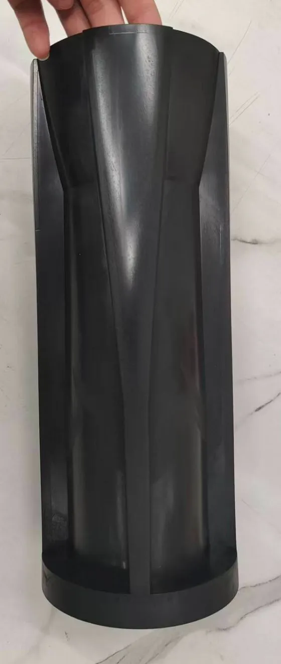 A first moulded black sleeve held up by its top on a marble table, showing its tapered channels and round base
