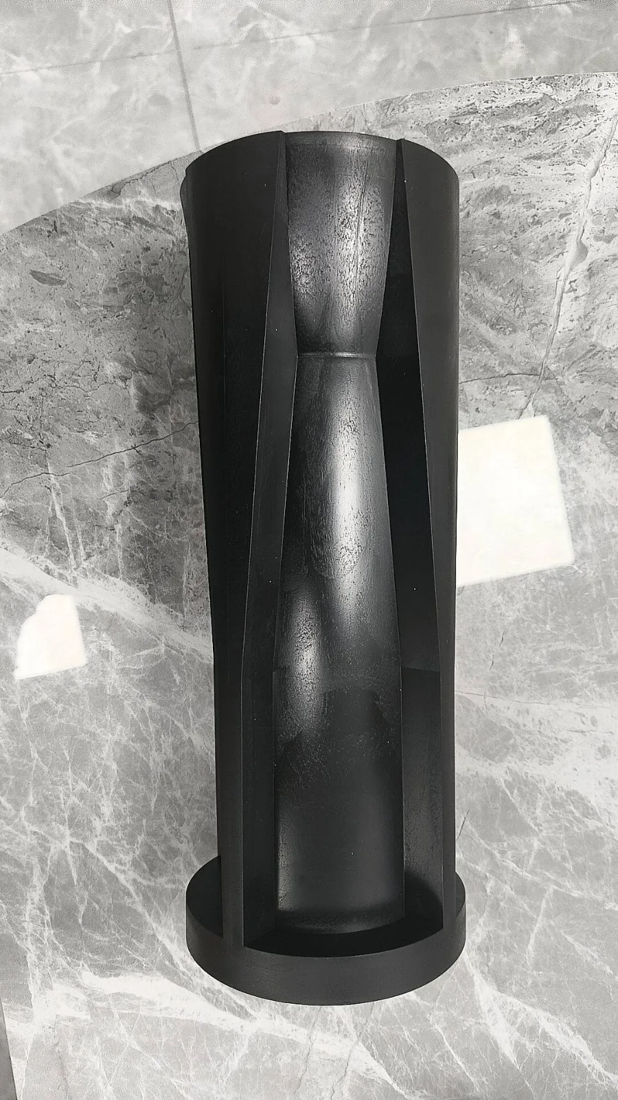 A single moulded sleeve on a grey marble table, seen from above, with a tapered channel running down one side