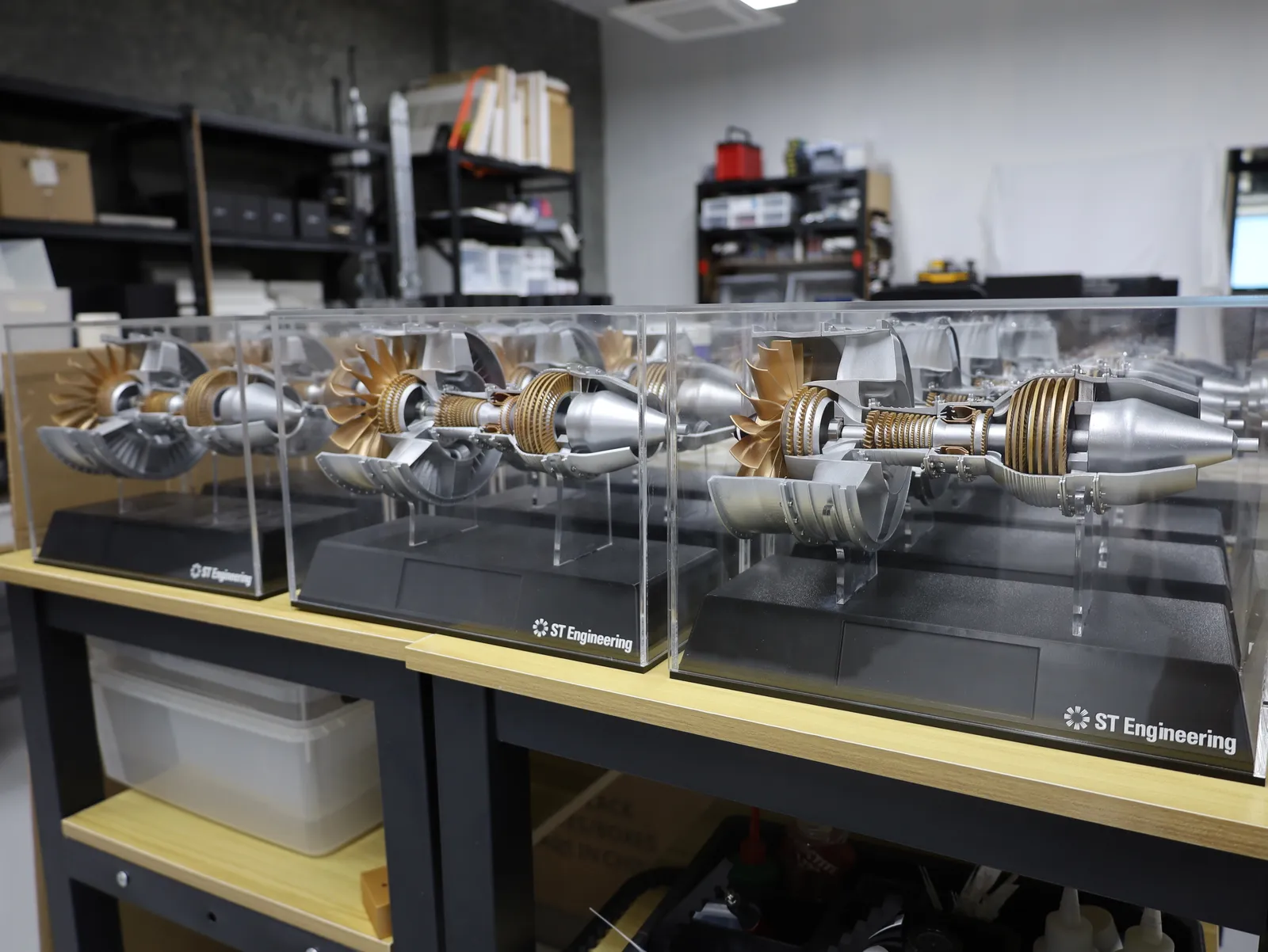 A row of finished jet engine models in clear acrylic cases on a workbench in our studio
