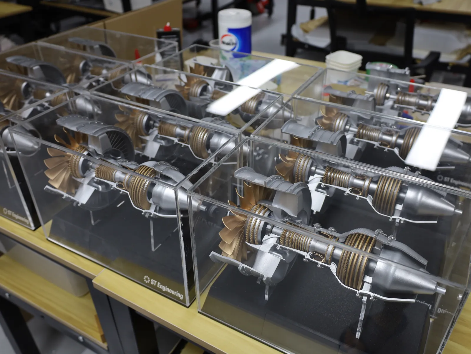 Several cased jet engine models seen from above, packed side by side on a workbench