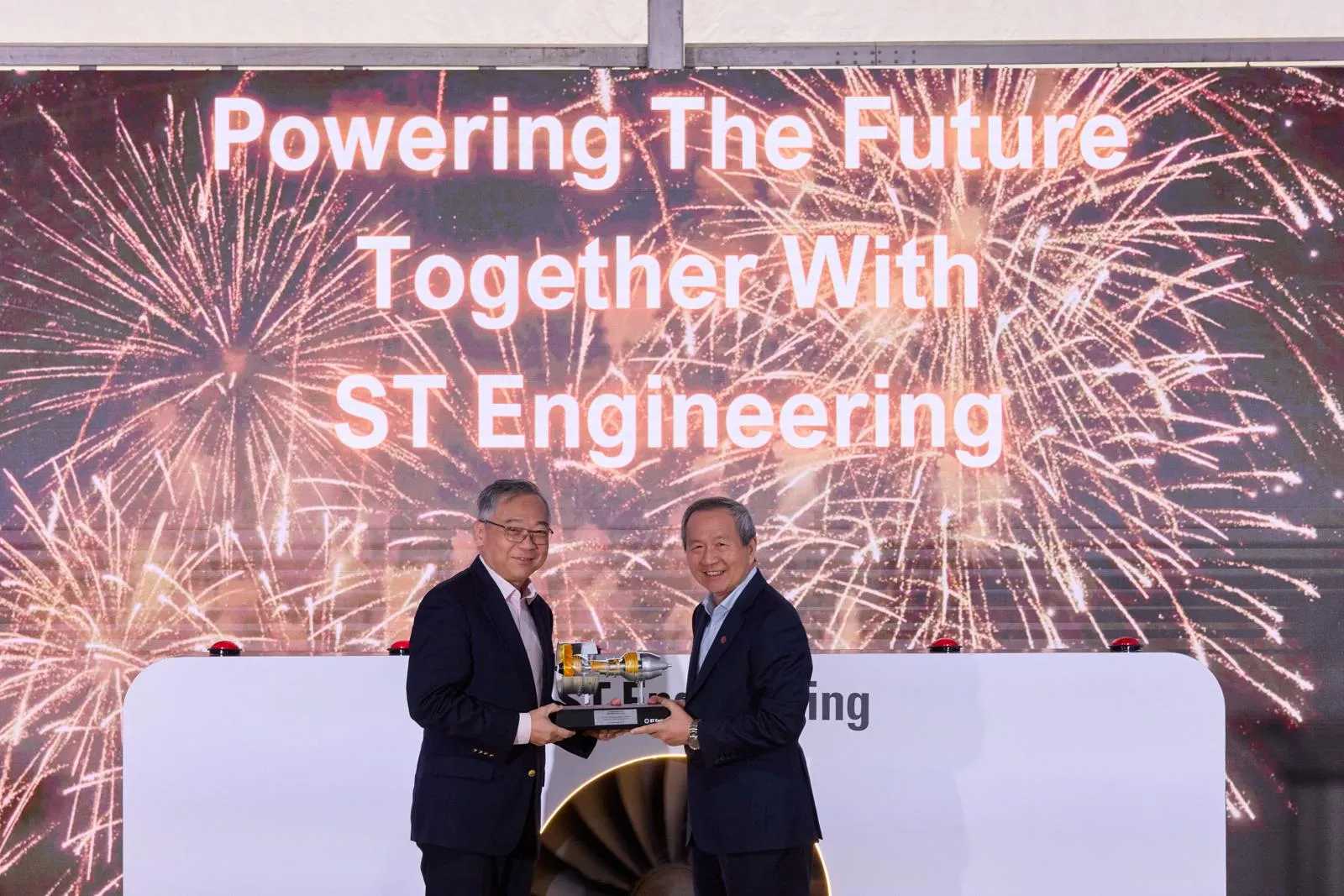 The guest of honour receiving the jet engine model on stage, in front of a backdrop reading Powering The Future Together With ST Engineering