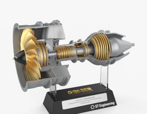 Render of the gold and silver engine on clear rods, with the Golden Years Ahead logo above a worded plate and the ST Engineering logo on the base