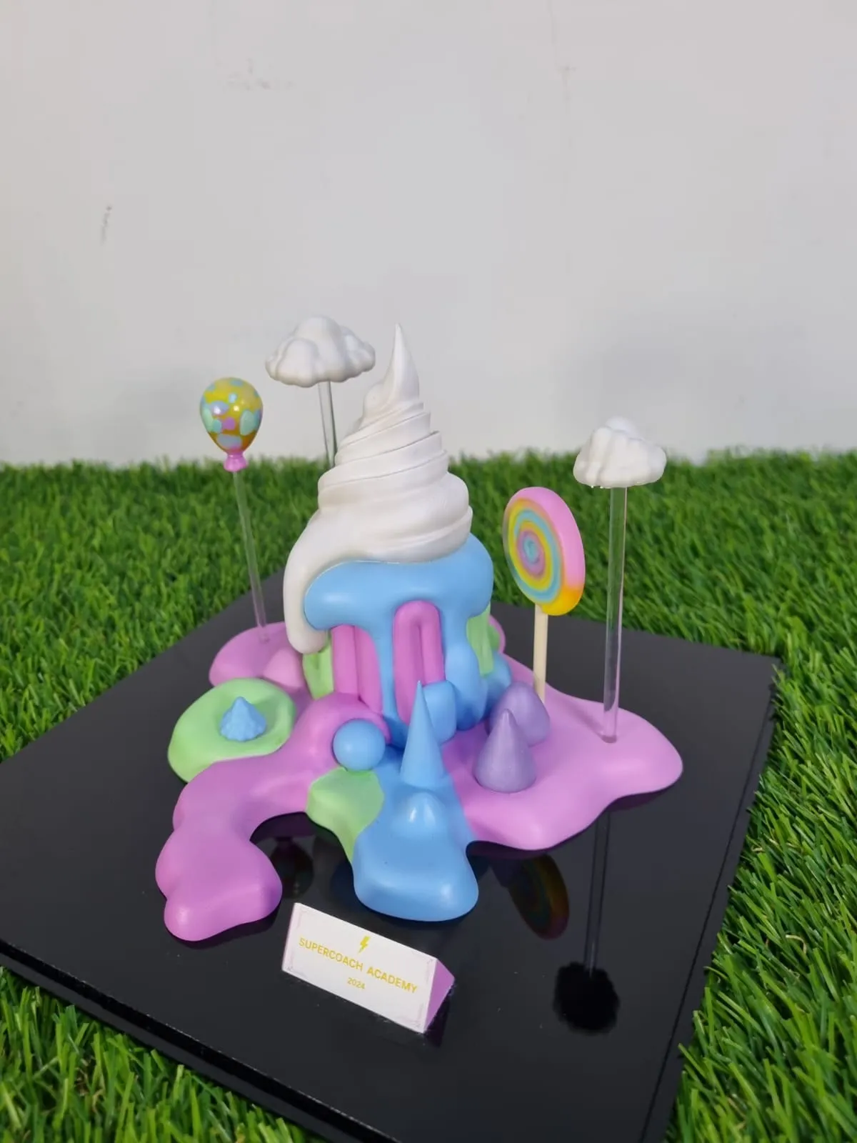 The cake trophy from a raised three-quarter angle, showing the pink, mint and blue drips spreading across the black base