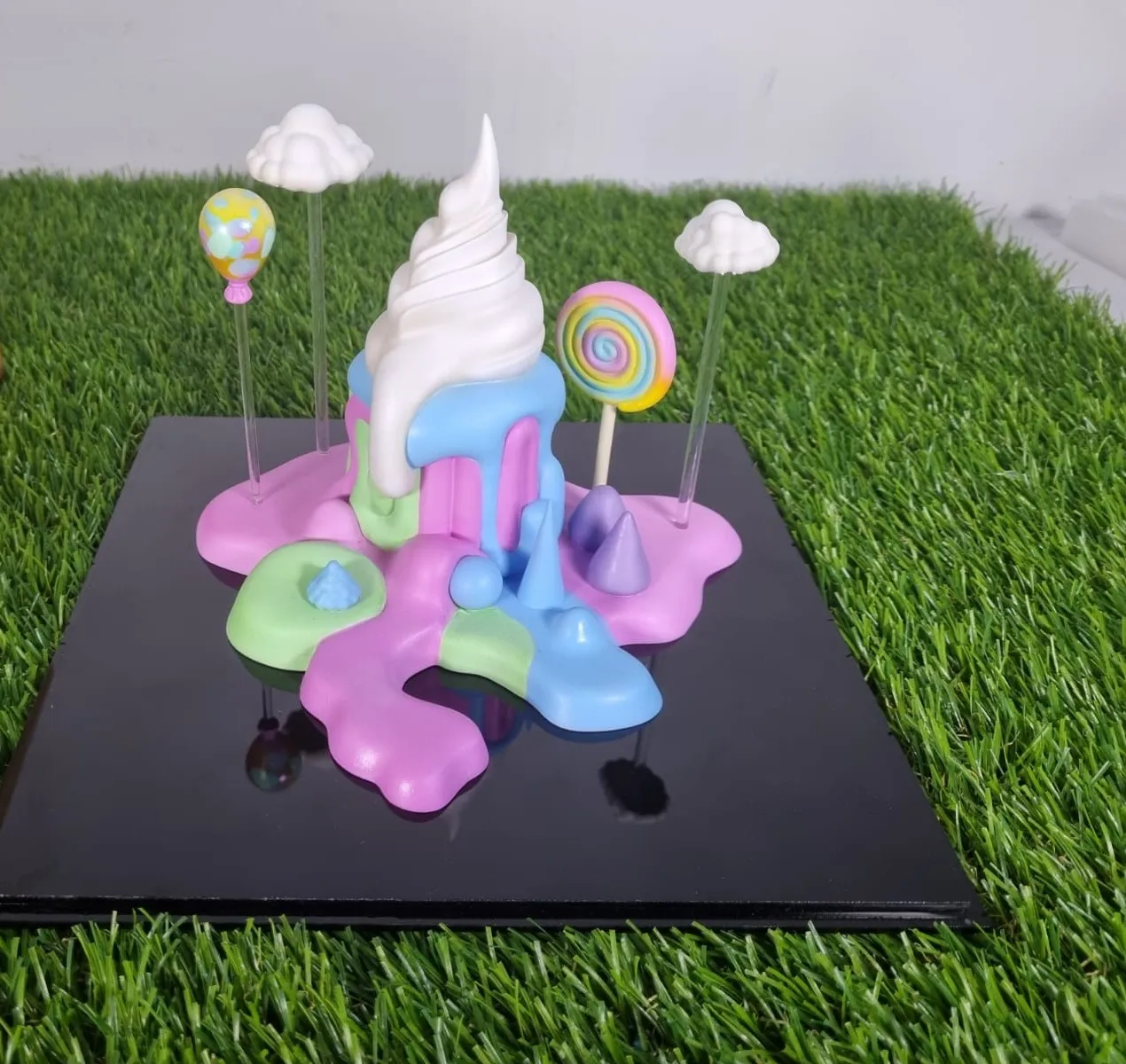 The cake trophy from the side, with the lollipop, the balloon and two clouds on clear rods around the swirl