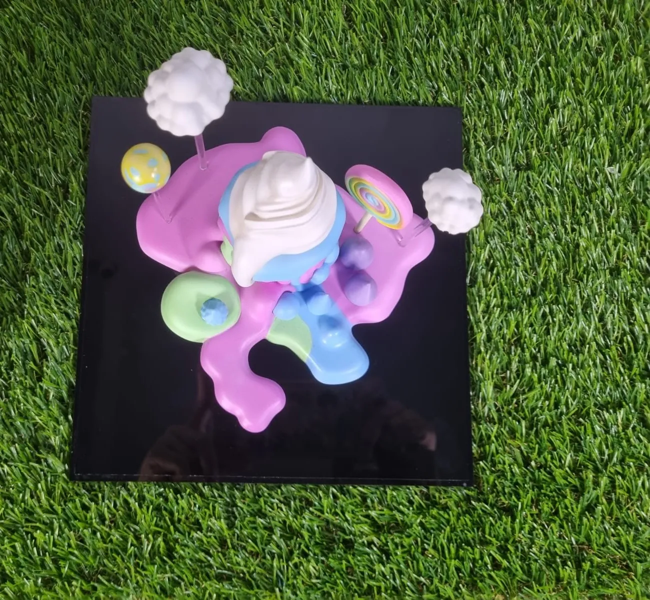 Top-down view of the cake trophy: the white swirl in the middle of pink, mint and blue drips on a square black base