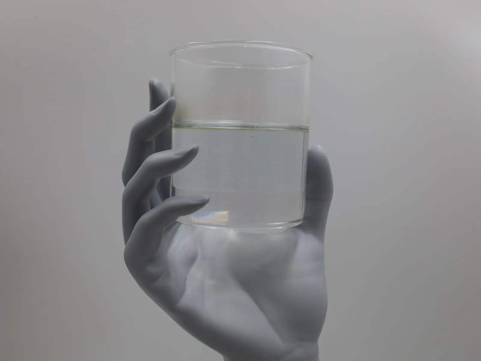 A sculpted grey hand with long fingers gripping a clear glass of water, half full