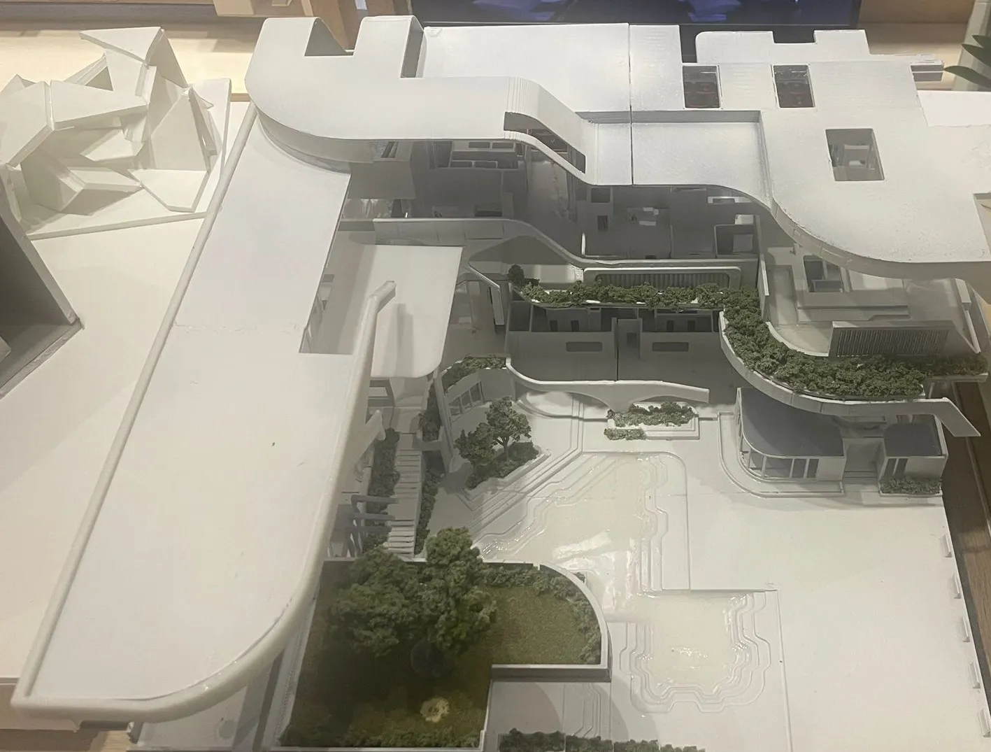 The model from above: a long curved roof, planted terraces stepping down and the white plaza below