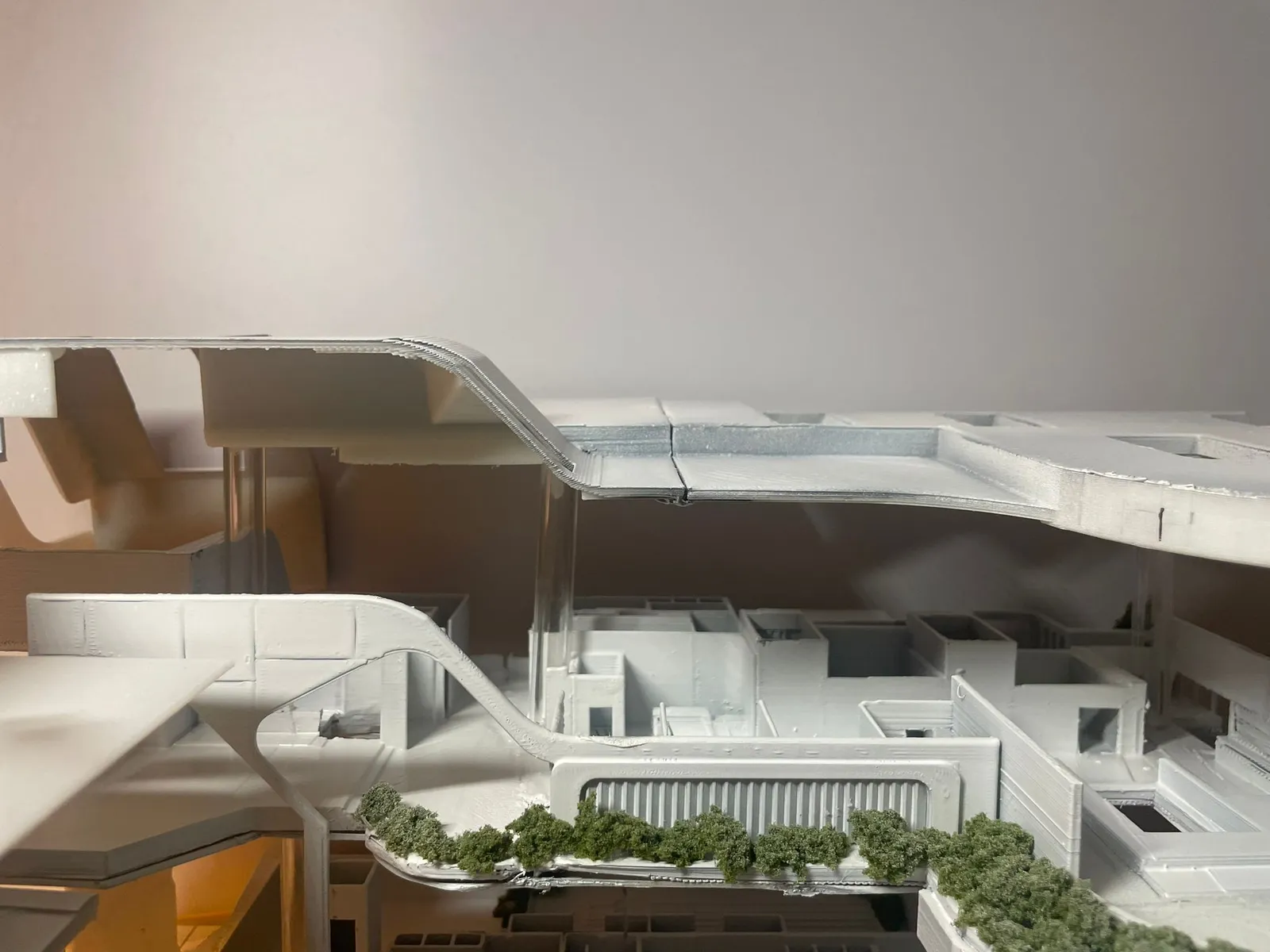 Side view between the levels: a clear acrylic column holding the curved roof above a floor of printed rooms and a planted ledge