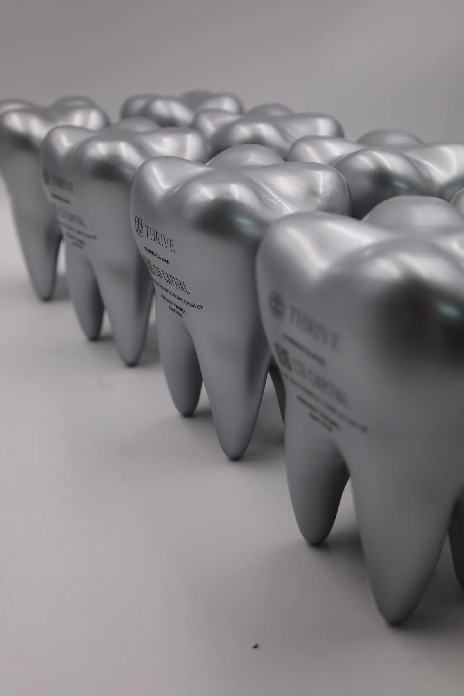 A row of silver tooth trophies seen from the side, each standing on its roots with the black printed logos on the front