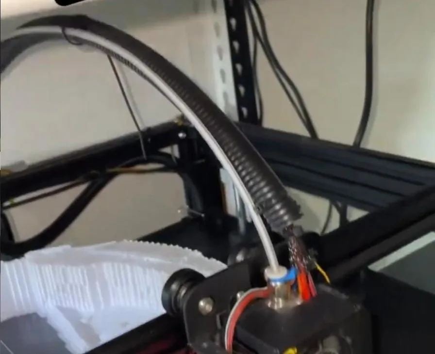 The print head of an FDM printer laying down a white part, with finished white prints beside it