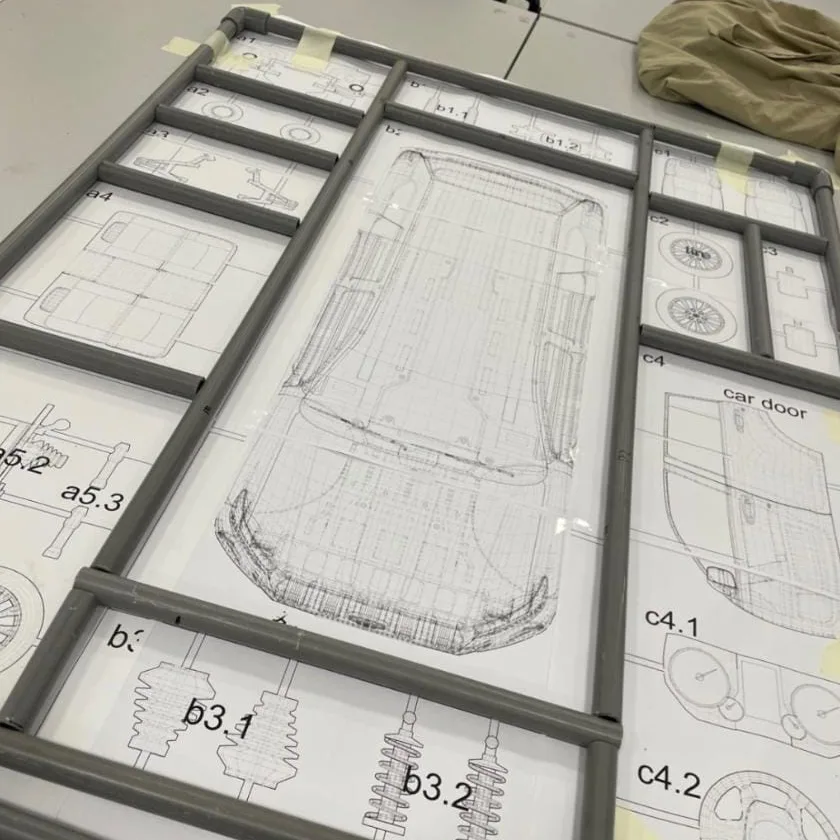 Grey pipe frames set over printed drawings of a car's parts, each part labelled