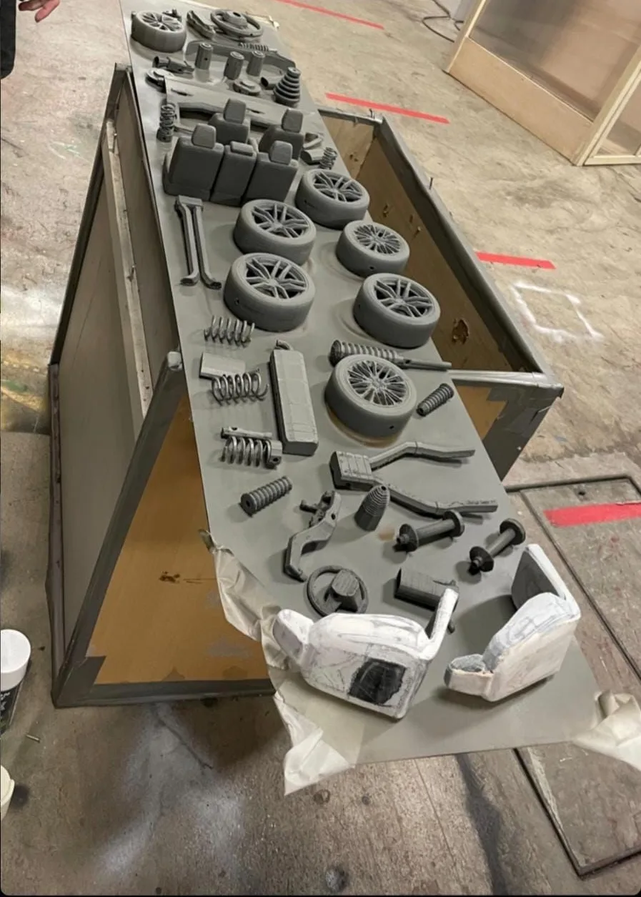 Printed seats, wheels, springs and pedals laid on a board, coated in grey primer