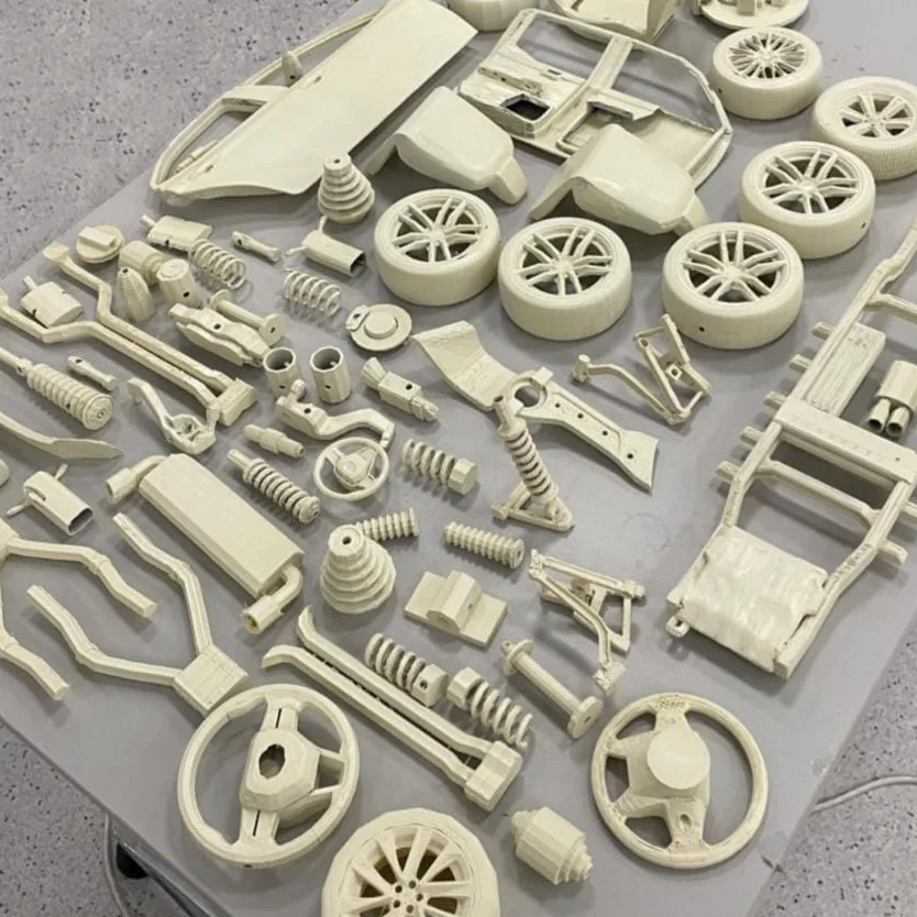 Wheels, steering wheels, springs and chassis parts sprayed off-white, laid out on a grey table to dry