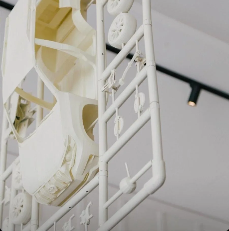 The underside of a hanging kit, the car body and a row of wheels on the frame, lit from the ceiling track