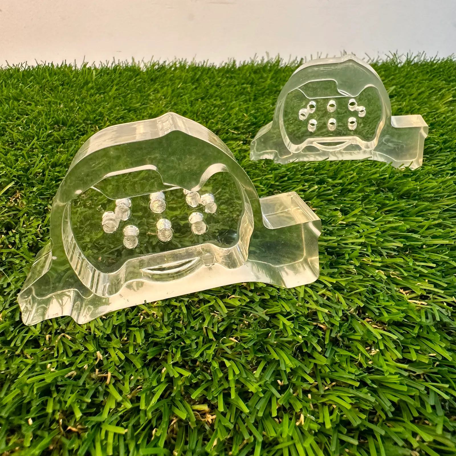 Two clear resin domes on artificial grass, the raised studs inside each one visible through the part