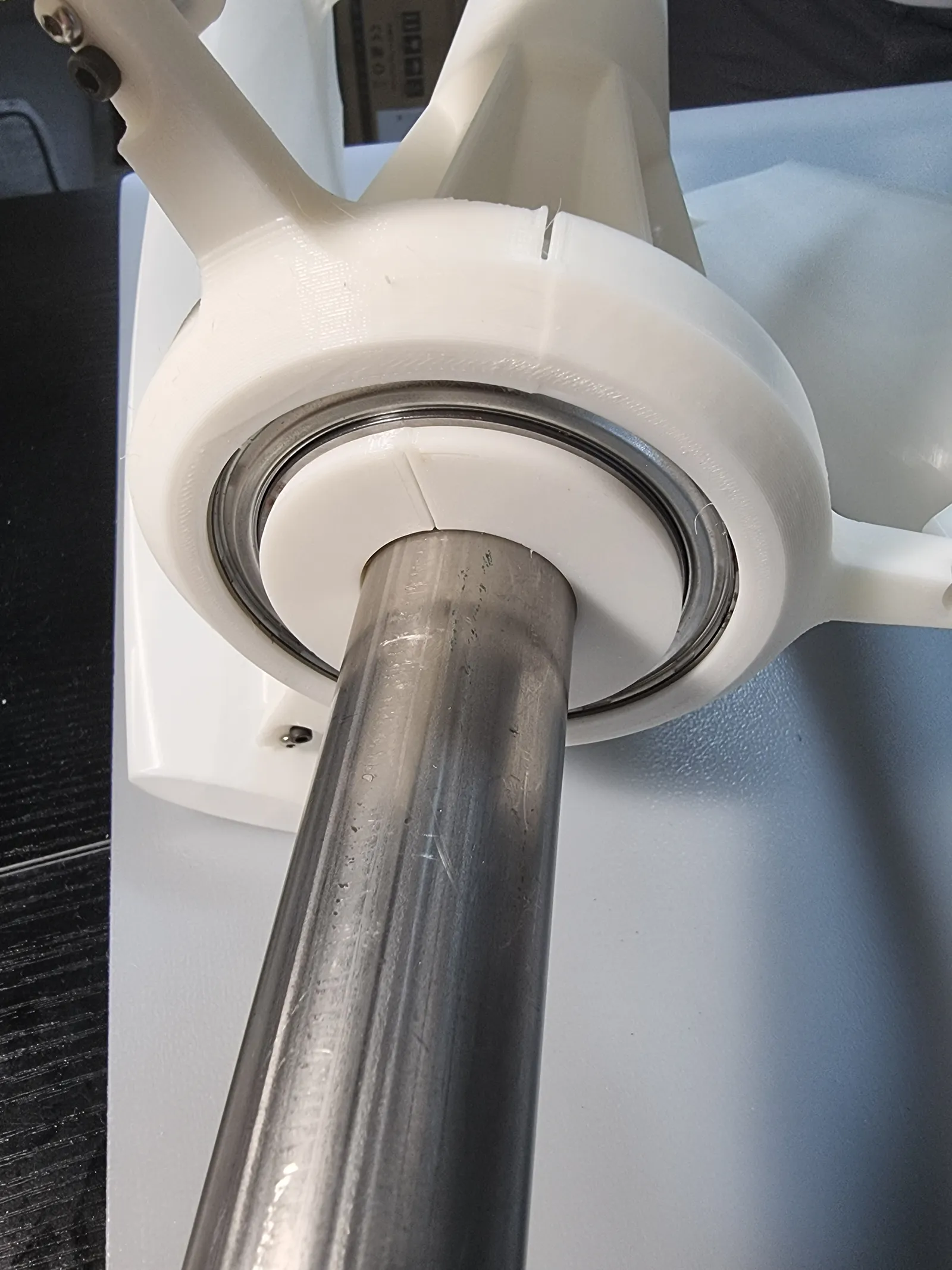 Close-up of a steel shaft passing through a ball bearing seated in a white printed housing at the base of the blade arms