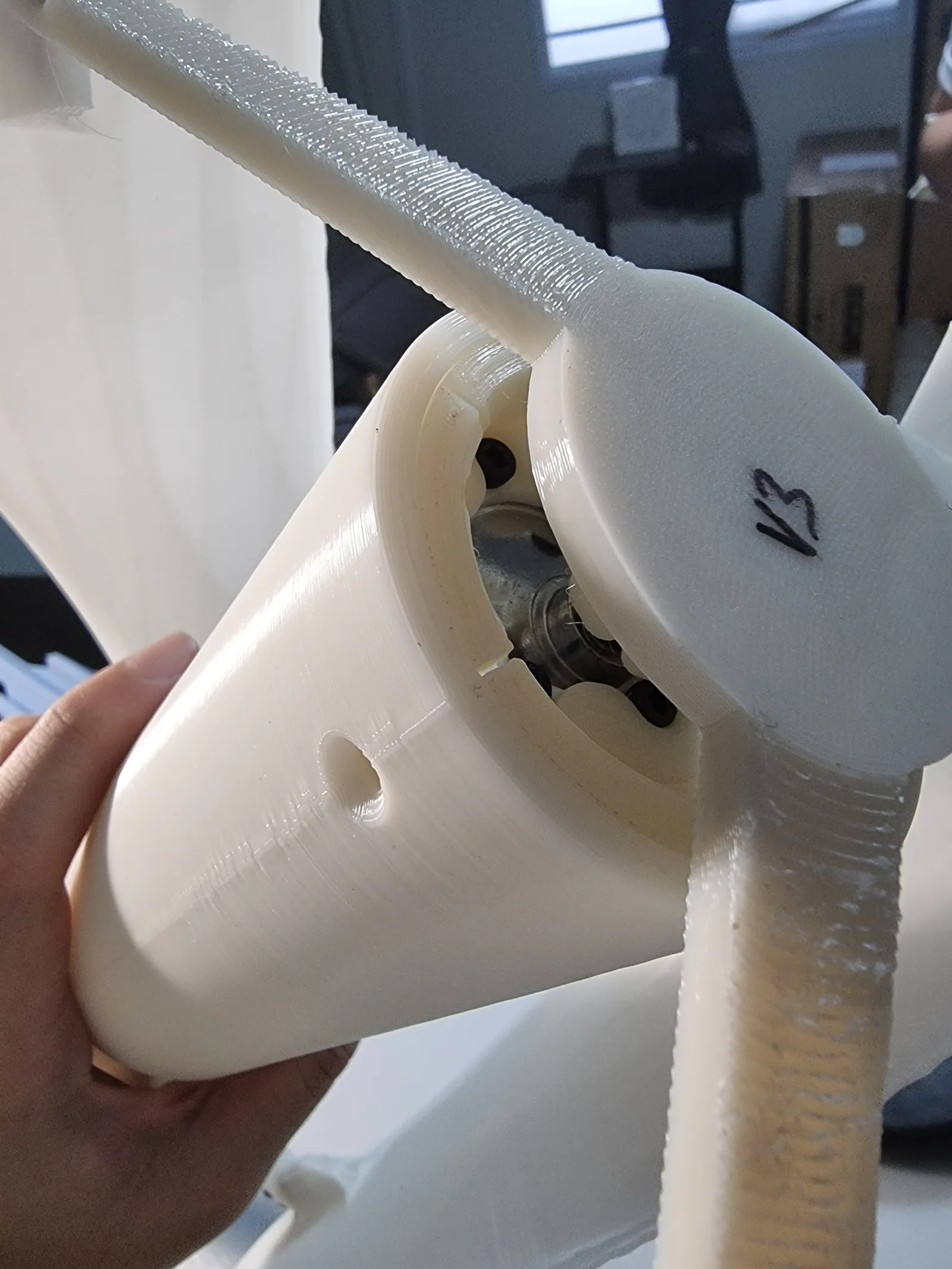 A hand holding the white printed hub, its cap marked V3, with two textured blade arms and screws visible inside